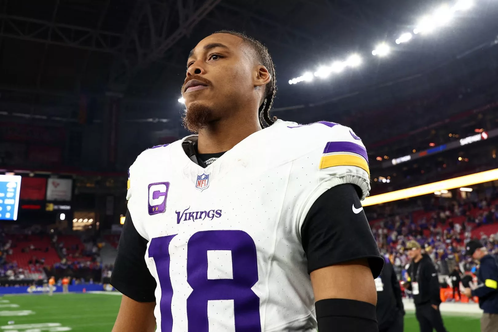 A focused NFL player in a Vikings jersey walks off the field, reflecting on the game amidst a vibrant stadium atmosphere